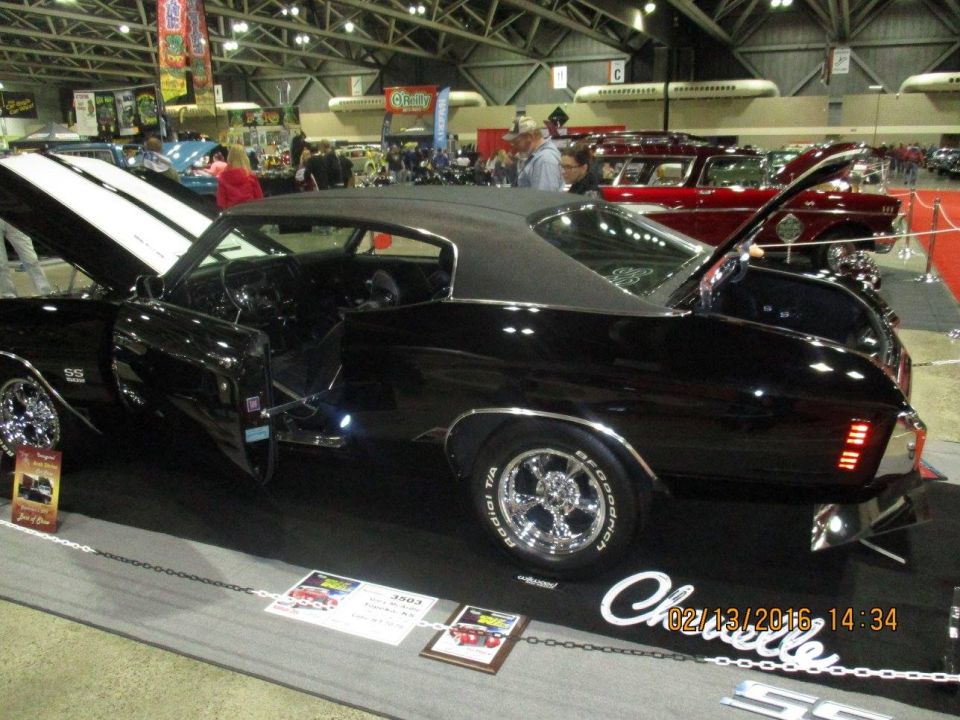 Black 1970 Chevrolet Chevelle SS with white racing stripes, hood and trunk open. Other cars visible in background