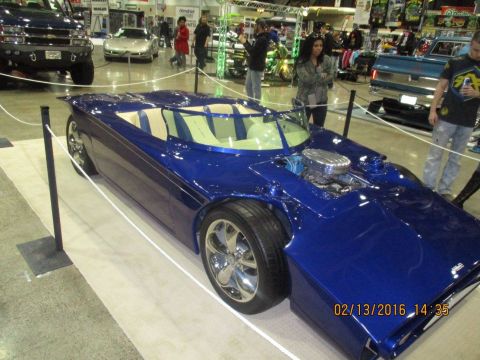 2004 Ford Crown Victoria - A custom blue sports car with a prominent chrome engine is displayed indoors, with other vehicles and people in the background.