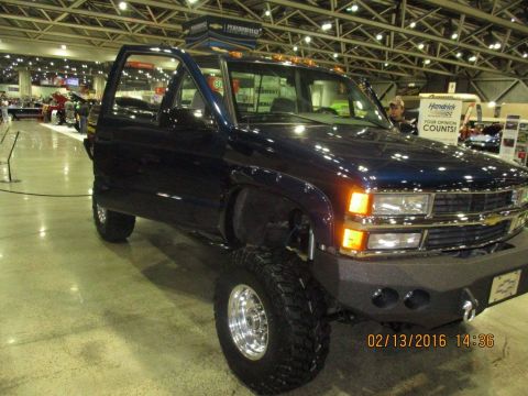 2004 Ford Crown Victoria - This dark blue pickup truck features a lifted suspension, aftermarket bumper, and chrome wheels, seen indoors at an event.