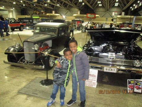 2004 Ford Crown Victoria - Two boys pose in front of a display of classic cars at an indoor event.