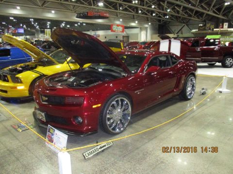 2004 Ford Crown Victoria - Red Chevrolet Camaro on display at an indoor car show, with a yellow Ford Mustang to its left.
