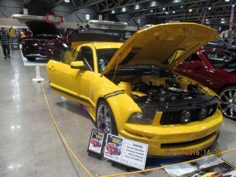 2004 Ford Crown Victoria - A yellow Ford Mustang is displayed with its hood and door open at an indoor event.
