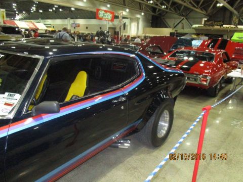 2004 Ford Crown Victoria - A black muscle car with distinctive tri-color racing stripes and bright yellow seats is displayed indoors alongside other vehicles.