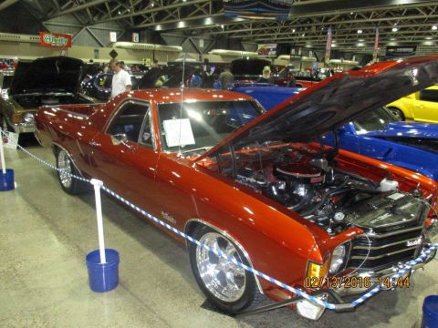 2004 Ford Crown Victoria - This orange pickup truck is on display at an indoor event with other vehicles around it.