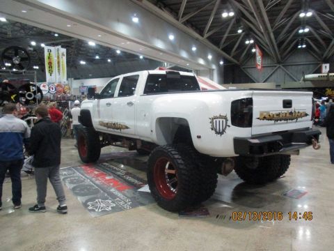 2004 Ford Crown Victoria - A heavily modified white dually pickup truck is displayed indoors with custom badging and large off-road tires.