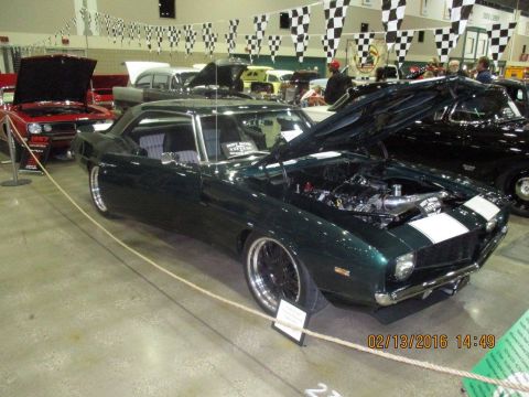 2004 Ford Crown Victoria - A dark green 1969 Chevrolet Camaro coupe is displayed with its hood open, revealing the engine bay.