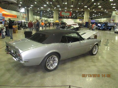 2004 Ford Crown Victoria - A silver convertible with its hood open is displayed indoors at a car show.