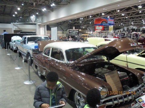 2004 Ford Crown Victoria - A classic Chevrolet sedan is displayed with its hood open at an indoor car show, alongside other vehicles.
