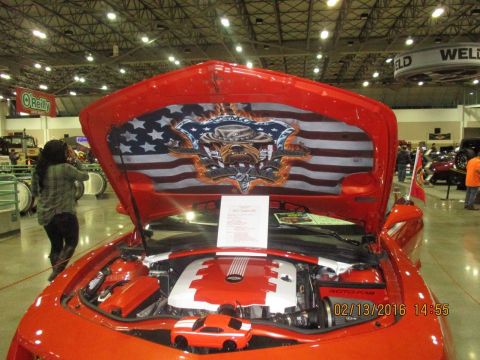 2004 Ford Crown Victoria - A red car is displayed with its hood open, revealing the engine and custom artwork of an American flag and a bulldog on the underside of th…