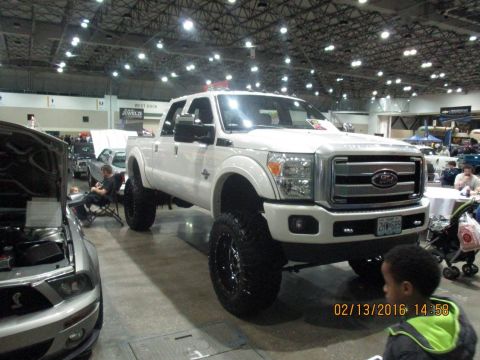 2004 Ford Crown Victoria - A lifted white Ford Super Duty pickup truck is displayed indoors, with another vehicle visible to its left.