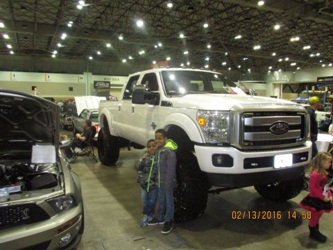 2004 Ford Crown Victoria - A lifted white Ford Super Duty pickup truck is displayed indoors, with two children posing in front of it.