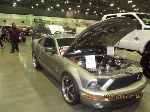 2004 Ford Crown Victoria - A silver Ford Mustang GT is displayed with its hood open at an indoor event, alongside other vehicles.