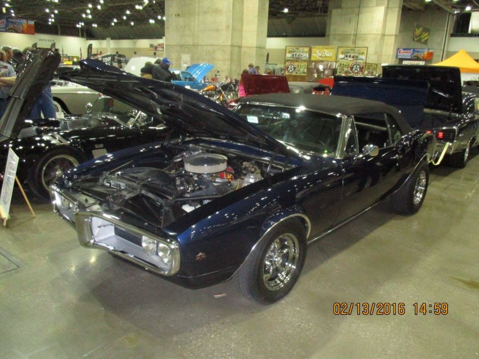 Dark blue 1967 Pontiac Firebird convertible with hood open, showing engine. Another car is parked behind it