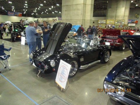 2004 Ford Crown Victoria - A black convertible sports car is displayed with its hood open, alongside other vehicles at an indoor event.