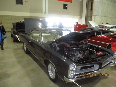 2004 Ford Crown Victoria - A dark classic car, possibly a 1965 model, is displayed with its hood open, revealing the engine compartment.