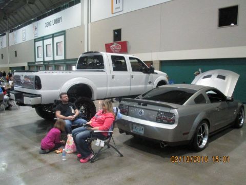 2004 Ford Crown Victoria - Two vehicles are displayed indoors with people watching.