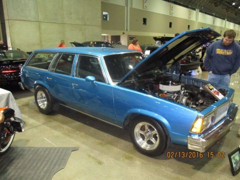 2004 Ford Crown Victoria - A blue station wagon is displayed with its hood open, revealing the engine and chrome grille, at an indoor event.