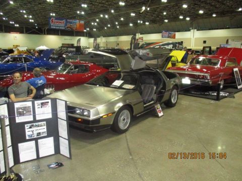 2004 Ford Crown Victoria - DeLorean DMC-12 displayed at a car show with its distinctive gullwing doors open.