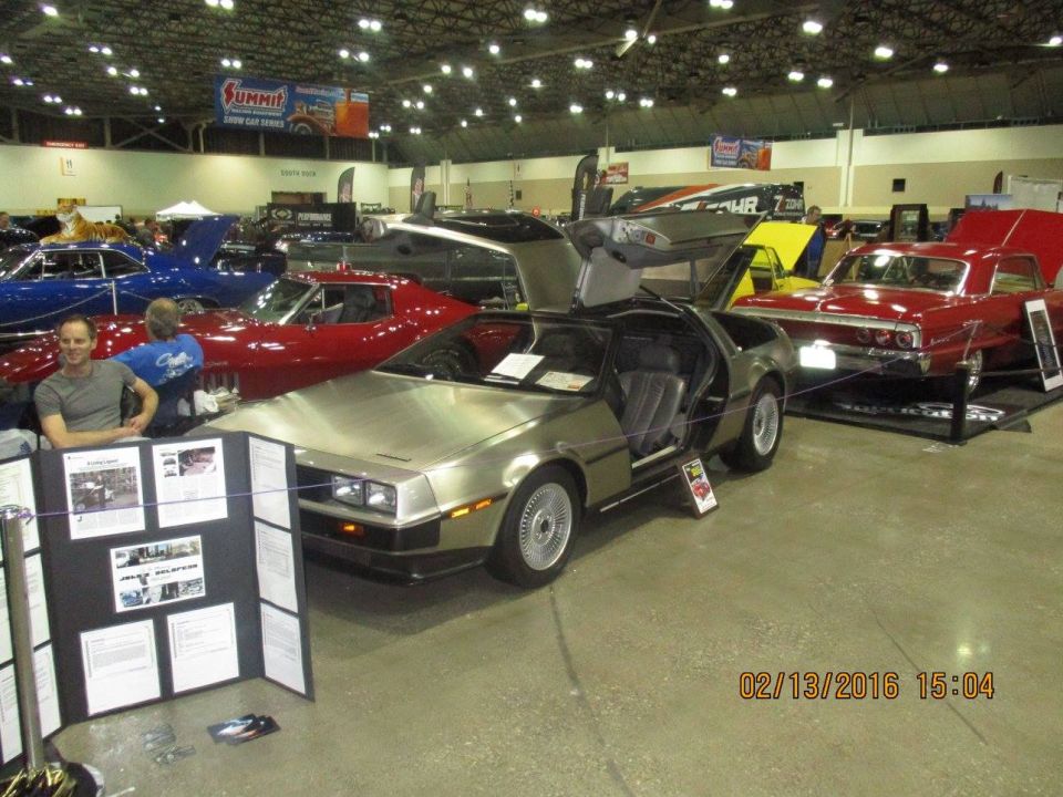 DeLorean DMC-12 with gullwing doors open, parked indoors next to other cars