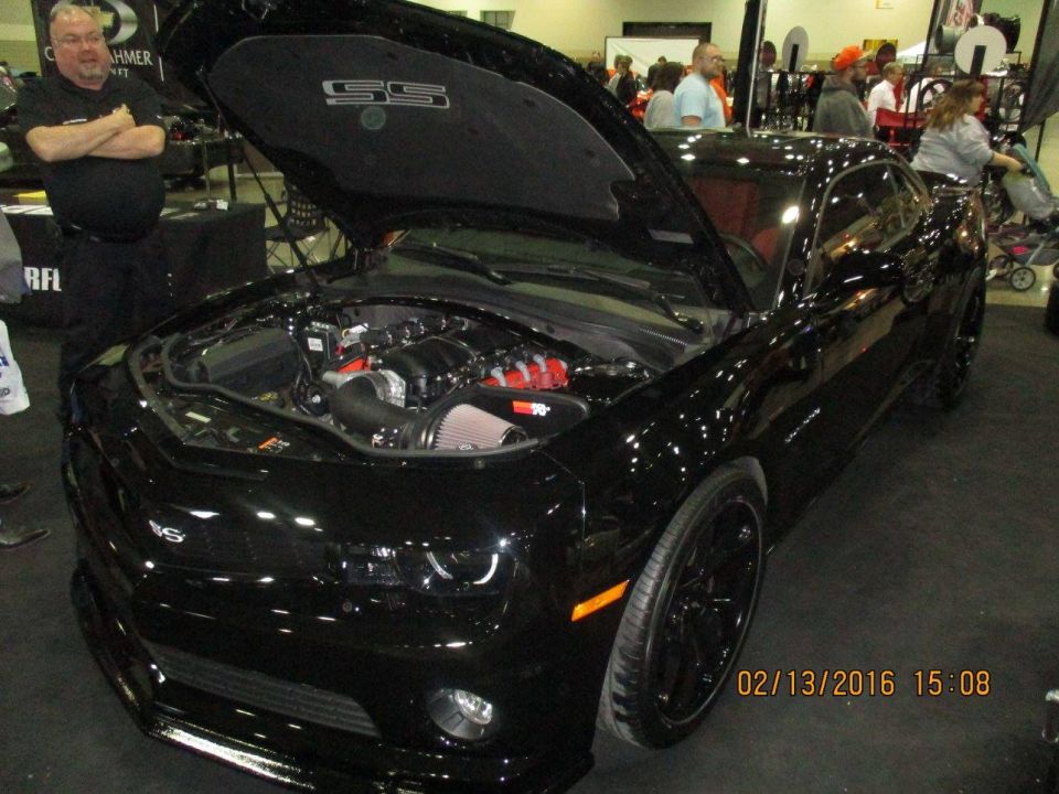 Black Chevrolet Camaro SS with hood open, showing engine. "SS" emblem visible on hood liner