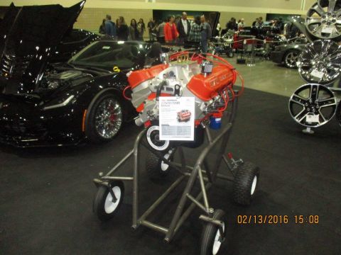 2004 Ford Crown Victoria - A V8 engine is displayed on a stand at an auto show, with a black sports car visible behind it.