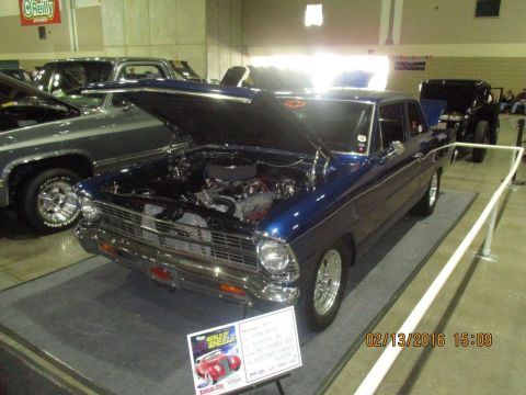 2004 Ford Crown Victoria - A classic blue Chevrolet Nova is displayed with its hood open at an indoor car show.