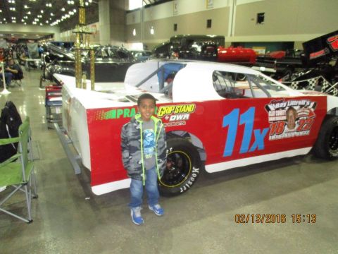 2004 Ford Crown Victoria - A young boy poses next to a race car at an indoor event, possibly a car show or race exhibition.