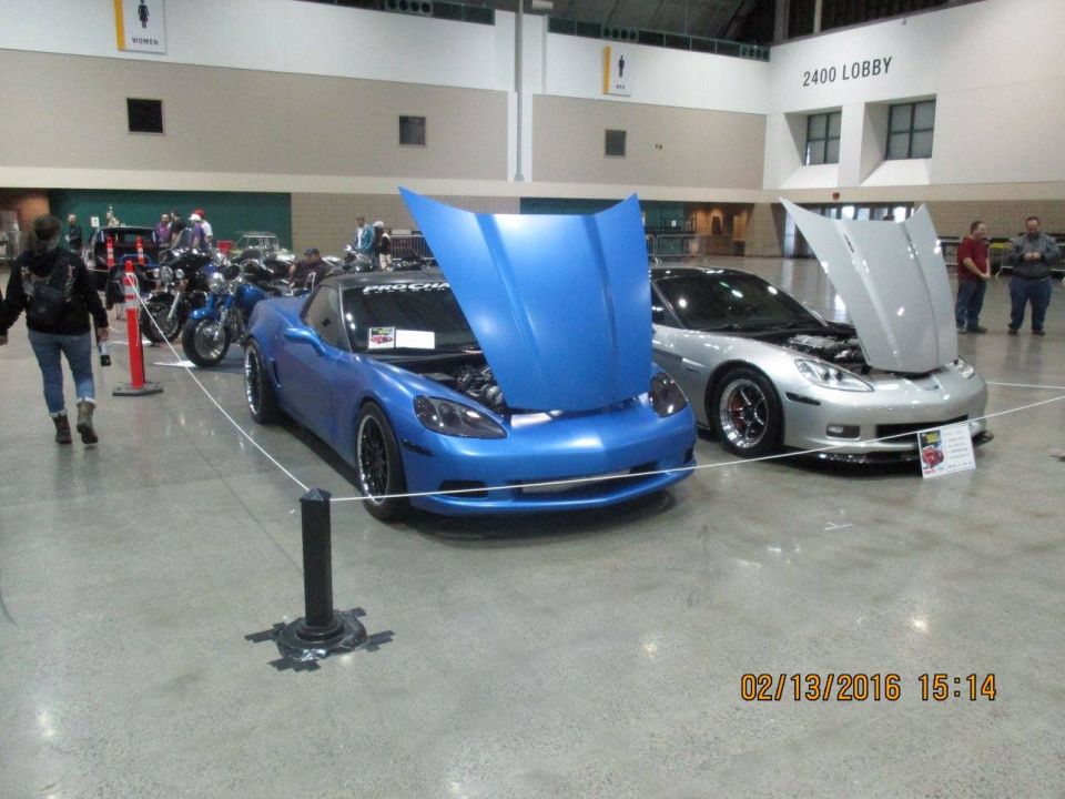 Blue and silver sports cars, hoods open, at an indoor car show