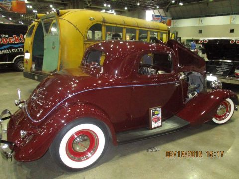 2004 Ford Crown Victoria - A maroon coupe with whitewall tires is displayed indoors next to a yellow bus and other vehicles.
