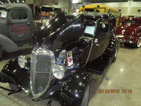 2004 Ford Crown Victoria - A black vintage sedan is displayed with its hood open, revealing the engine compartment. Other vehicles are visible in the background at an…