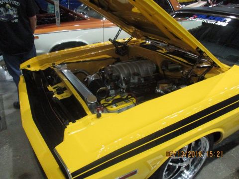 2004 Ford Crown Victoria - The engine bay of a custom yellow muscle car is displayed, a prominent supercharger and racing stripes.