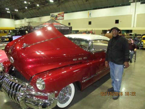 2004 Ford Crown Victoria - A man stands next to a red 1953 Buick Roadmaster convertible at a car show.