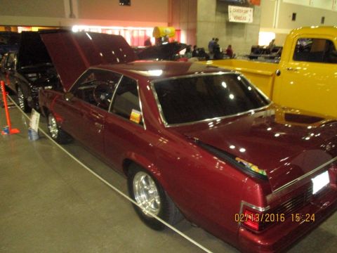 2004 Ford Crown Victoria - A maroon coupe is displayed with its hood and trunk open, next to a yellow pickup truck.