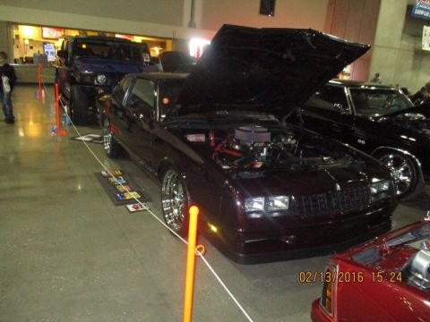 2004 Ford Crown Victoria - A dark red coupe with its hood open, revealing the engine, is displayed indoors next to other vehicles.