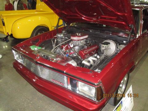 2004 Ford Crown Victoria - Customized red Chevrolet coupe on display with its engine exposed, next to a yellow pickup truck.