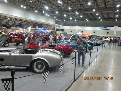 2004 Ford Crown Victoria - Indoor car show features multiple classic sports cars and a man posing for a photo.