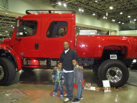 2004 Ford Crown Victoria - Man and two boys pose in front of a large red truck at an indoor event.