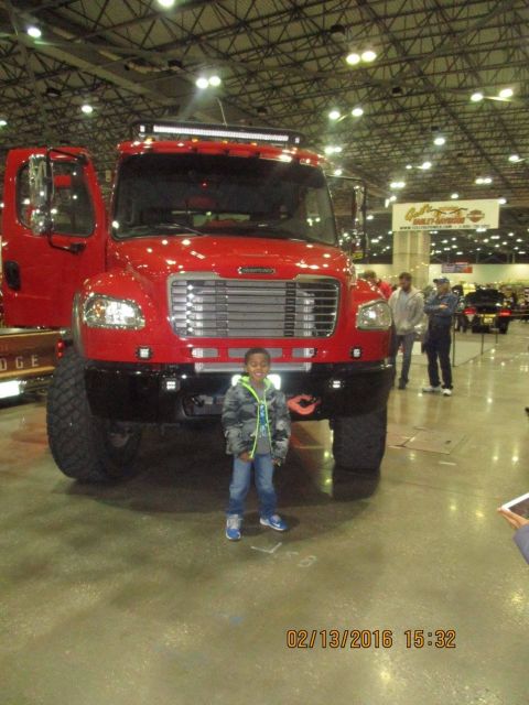 2004 Ford Crown Victoria - A child poses in front of a large red truck at an indoor event.