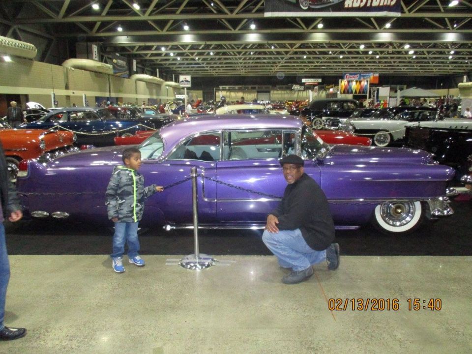 Man and kid by a purple classic car at a show. Other cars in background