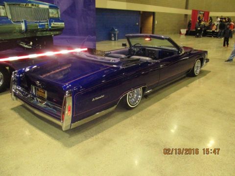 2004 Ford Crown Victoria - A custom purple convertible lowrider is displayed indoors, with another vehicle partially visible to the left.