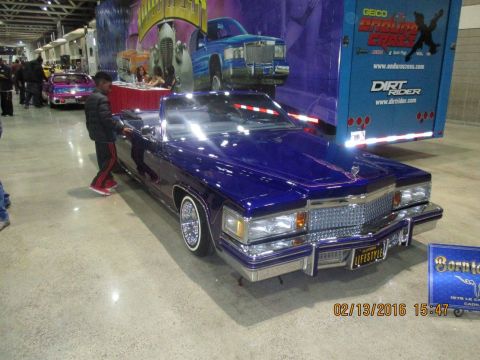 2004 Ford Crown Victoria - A custom purple 1979 Cadillac Coupe DeVille convertible is displayed indoors with a trailer in the background.