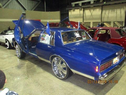 2004 Ford Crown Victoria - A custom blue sedan is displayed with its doors open, large chrome wheels and decorative flags.