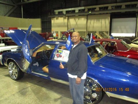 2004 Ford Crown Victoria - A man poses with a custom blue sedan at an indoor car show.