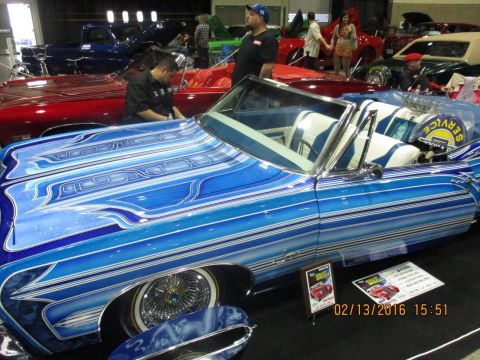 2004 Ford Crown Victoria - A heavily customized blue convertible with intricate pinstriping is displayed indoors alongside other vehicles.