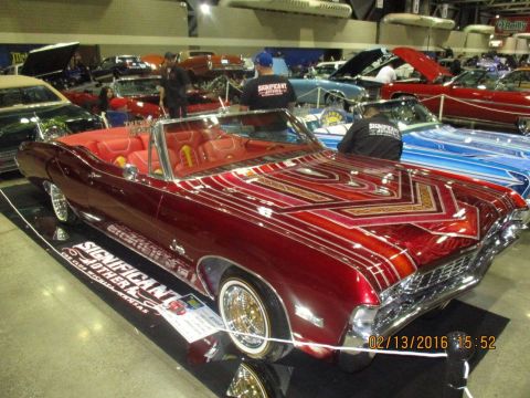 2004 Ford Crown Victoria - A custom red convertible with intricate pinstripe graphics is displayed at a car show.