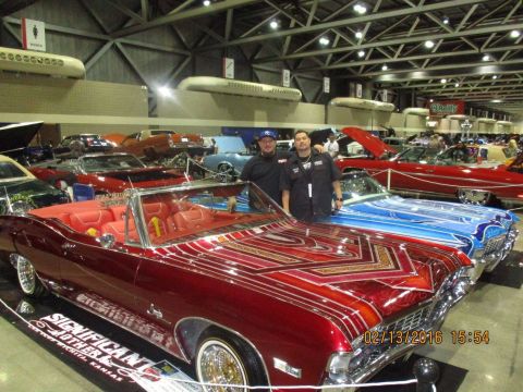 2004 Ford Crown Victoria - Two men stand beside customized lowrider cars at a car show.