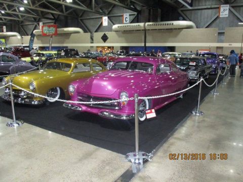2004 Ford Crown Victoria - A vibrant pink custom hot rod is displayed indoors alongside other vehicles.