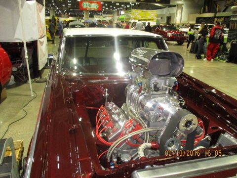 2004 Ford Crown Victoria - A heavily modified hot rod with a prominent supercharger is displayed indoors, with other vehicles and people in the background.
