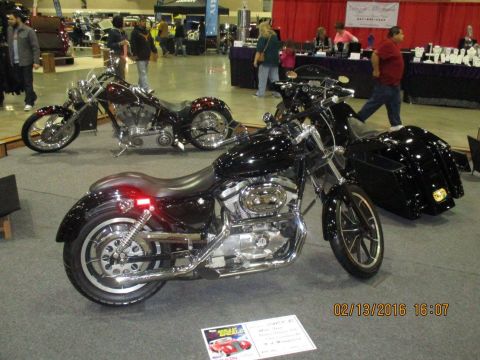 2004 Ford Crown Victoria - Two motorcycles are displayed indoors at an event, with a sign in the foreground and people in the background.