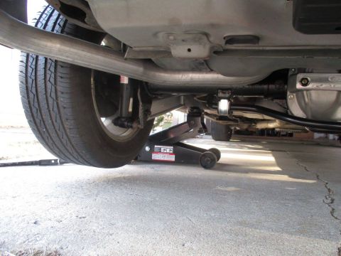 2004 Ford Crown Victoria - A vehicle's undercarriage is shown as it is raised on a hydraulic jack, revealing the exhaust system and rear suspension.
